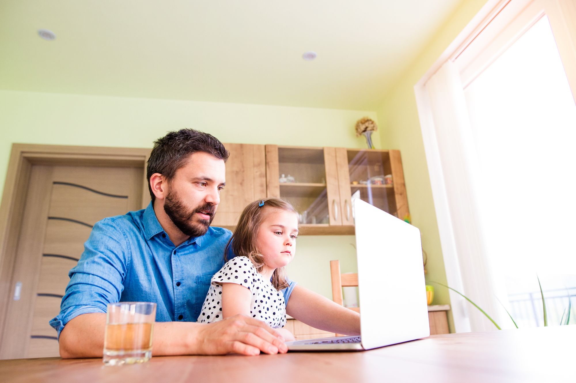 A father and daughter take an online class together while sitting at their kitchen table